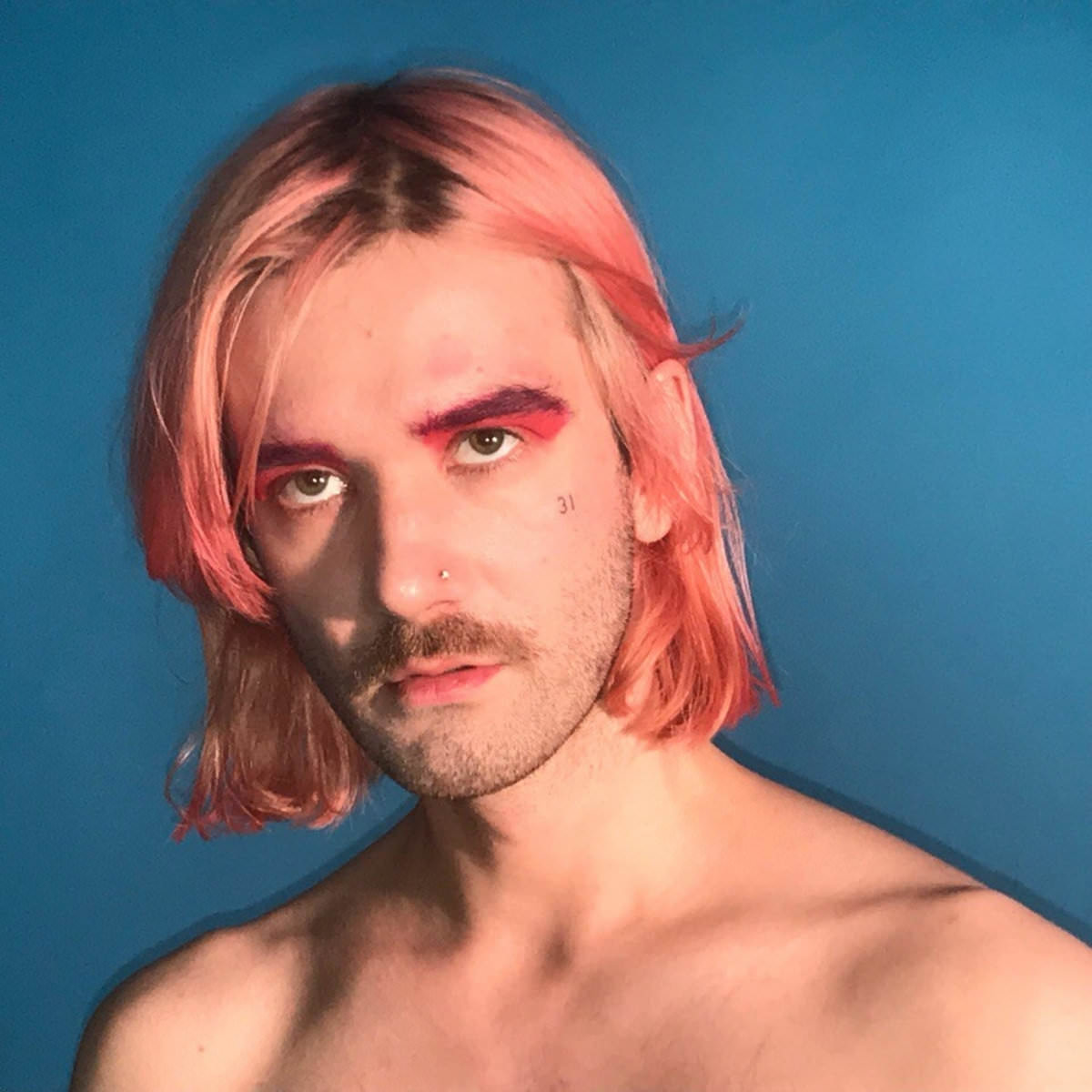 Фотография исполнителя Арсений Креститель. У него розовые волосы, лёгкий макияж и небритая щетина.